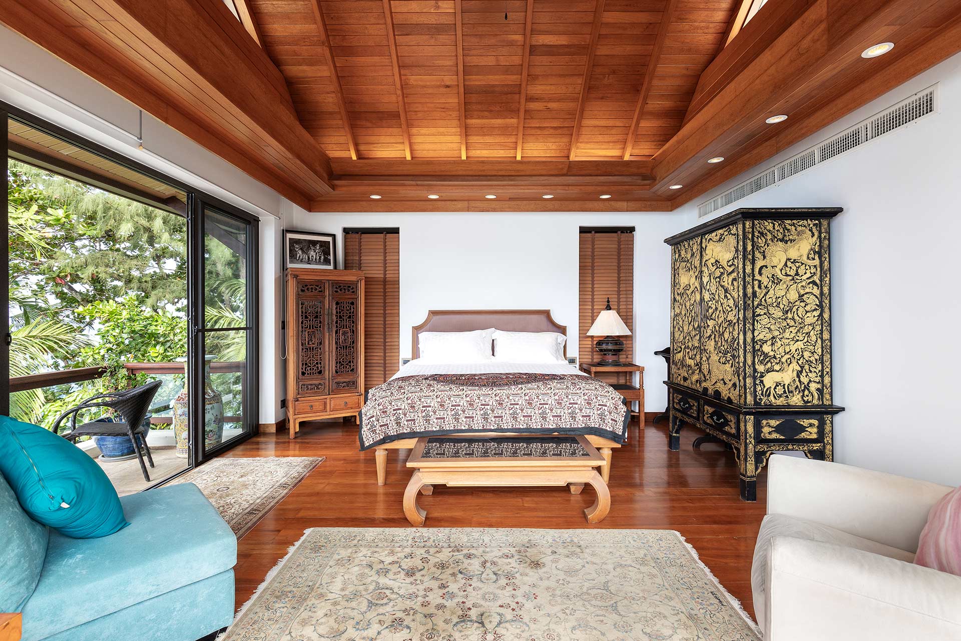 Bedroom with a wood-paneled ceiling, large bed at center, and antique carved cabinets on both sides; sliding glass doors open to a balcony on the left.