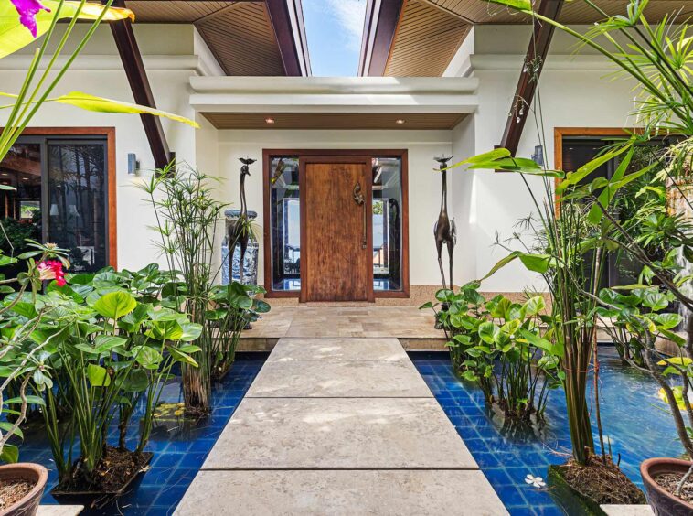 Entry courtyard with a wooden front door, glass sidelights, and lush tropical plants surrounding a blue-tiled water feature.