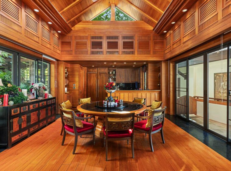 Luxurious wood-paneled dining room with a round wooden table and cushioned chairs, flanked by tall cabinets and large glass doors