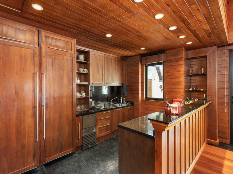 Rustic kitchen with tall wooden cabinets, open shelves, and a dark granite island.