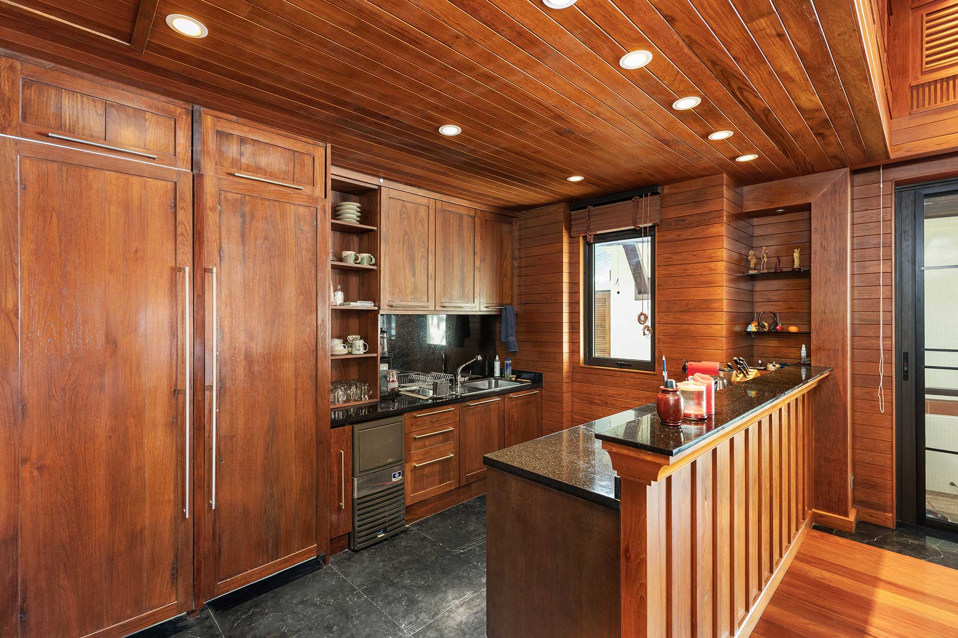 Rustic kitchen with tall wooden cabinets, open shelves, and a dark granite island.