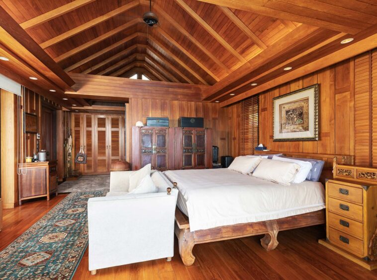Rustic master bedroom with vaulted wooden ceiling, paneled walls, and a large, white-ensemble bed.
