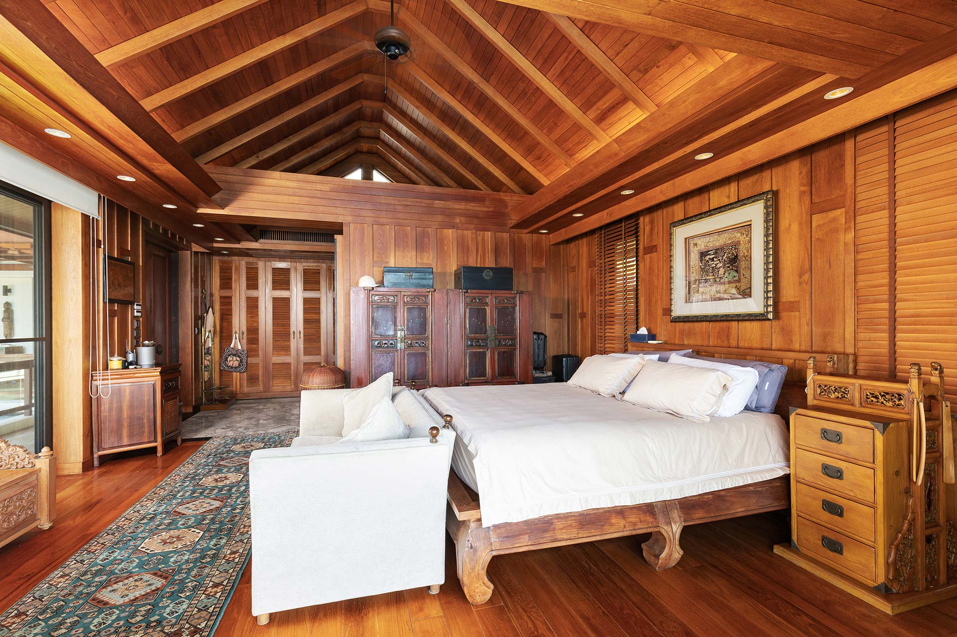 Rustic master bedroom with vaulted wooden ceiling, paneled walls, and a large, white-ensemble bed.