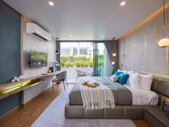 Modern hotel bedroom with a king bed, gray tones, teal accent wall, and wall-mounted TV overlooking a garden balcony.