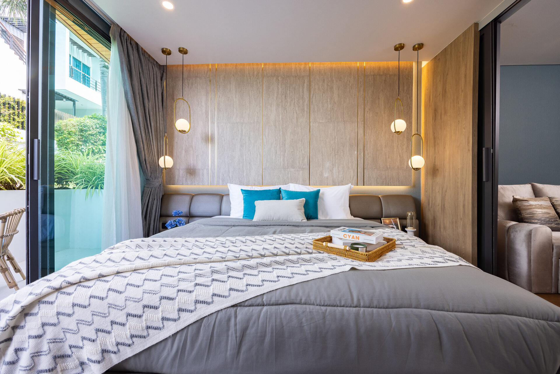 Modern hotel bedroom with a gray upholstered headboard, white and teal pillows, and a zigzag throw on a king bed.