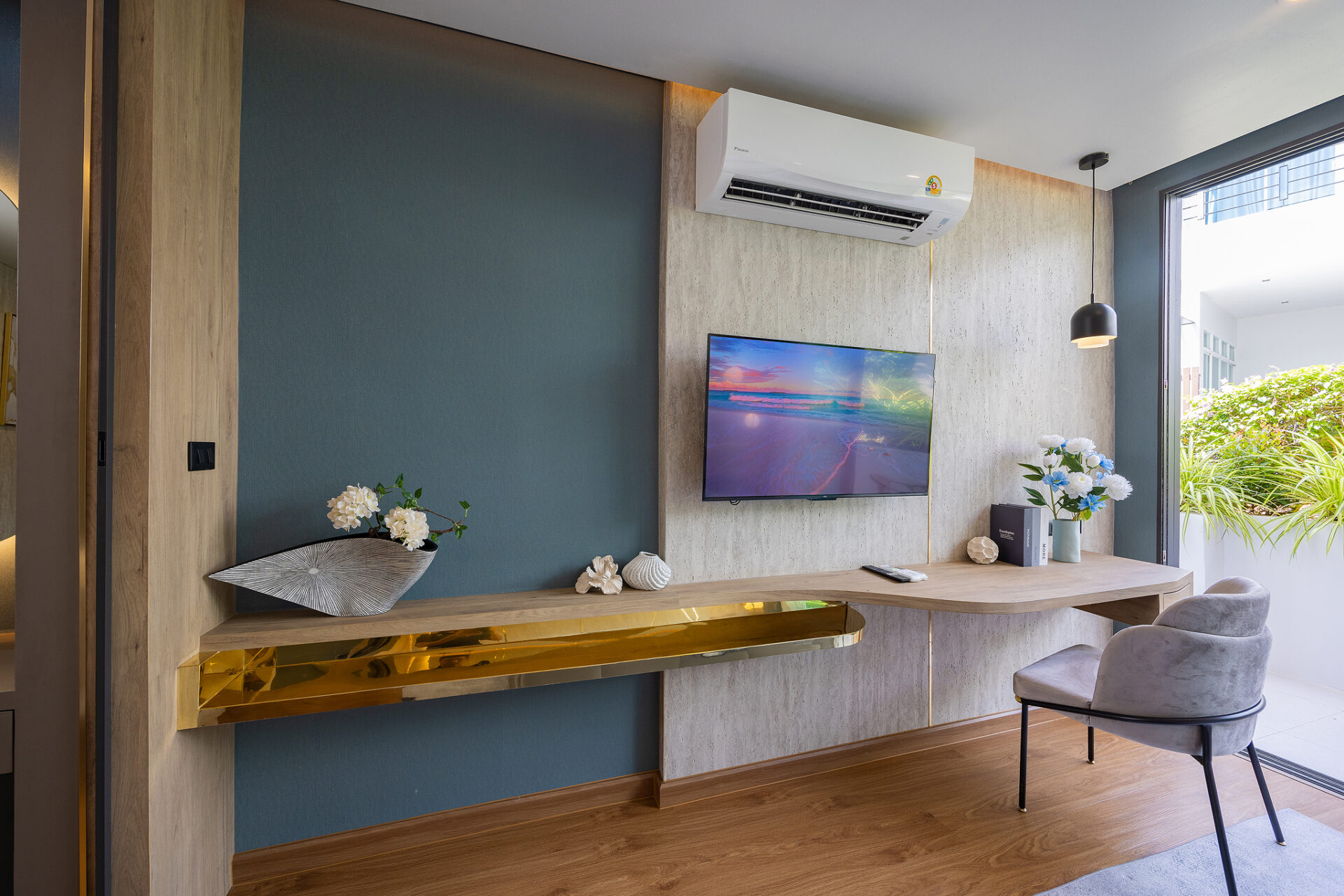 Modern living room with a wall-mounted TV, ceiling air conditioner, blue accent wall, wooden desk, and a gold decorative shelf along the wall.