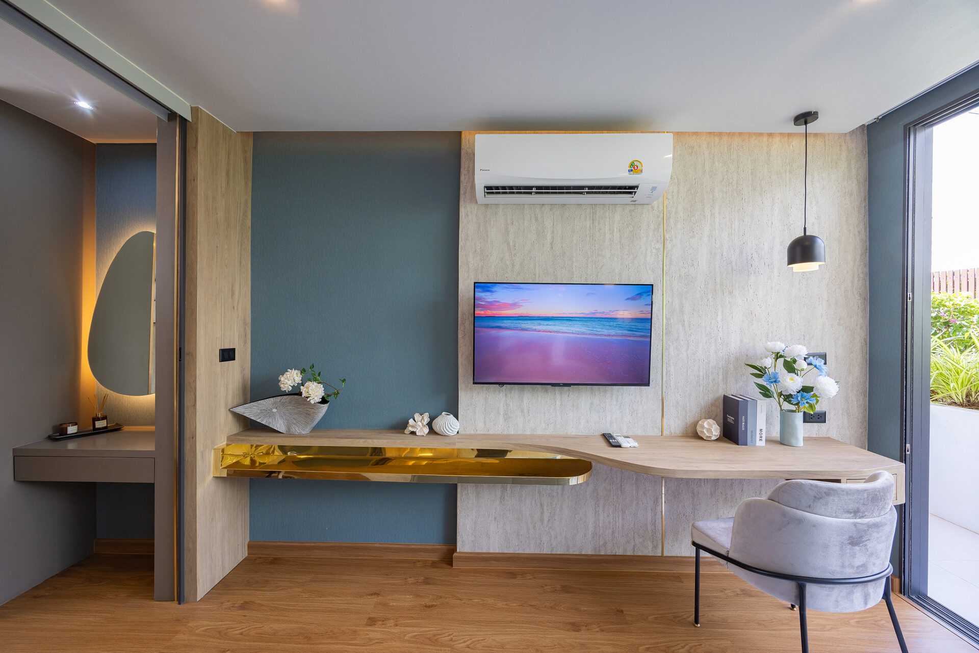 Modern living area with a wall-mounted TV, white air conditioner, blue and beige walls, and a wooden desk with a gold shelf.