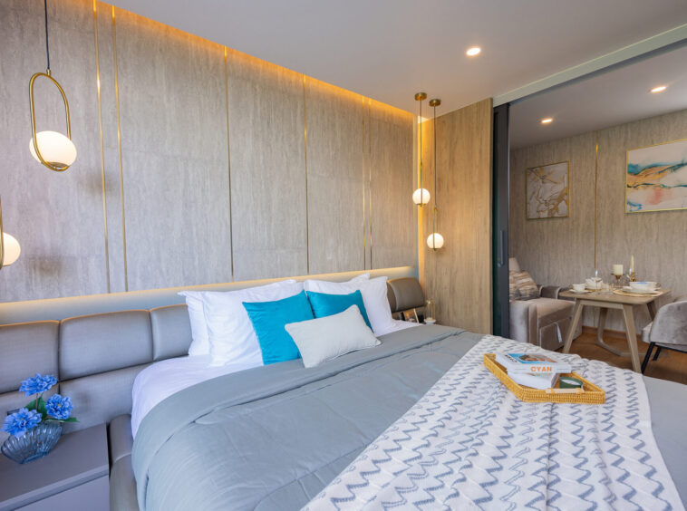 Modern hotel bedroom with a gray upholstered bed, blue and white pillows, and a chevron-patterned throw; brass globe pendant lights above.
