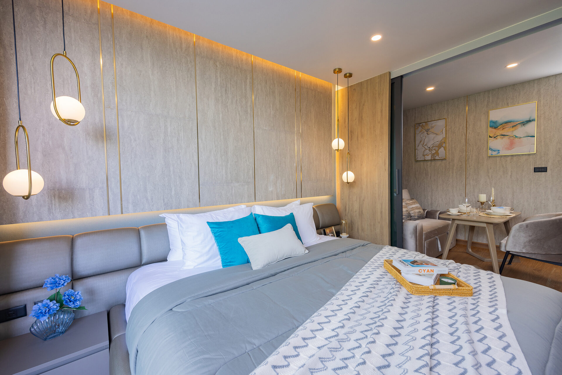 Modern hotel bedroom with a gray upholstered bed, blue and white pillows, and a chevron-patterned throw; brass globe pendant lights above.