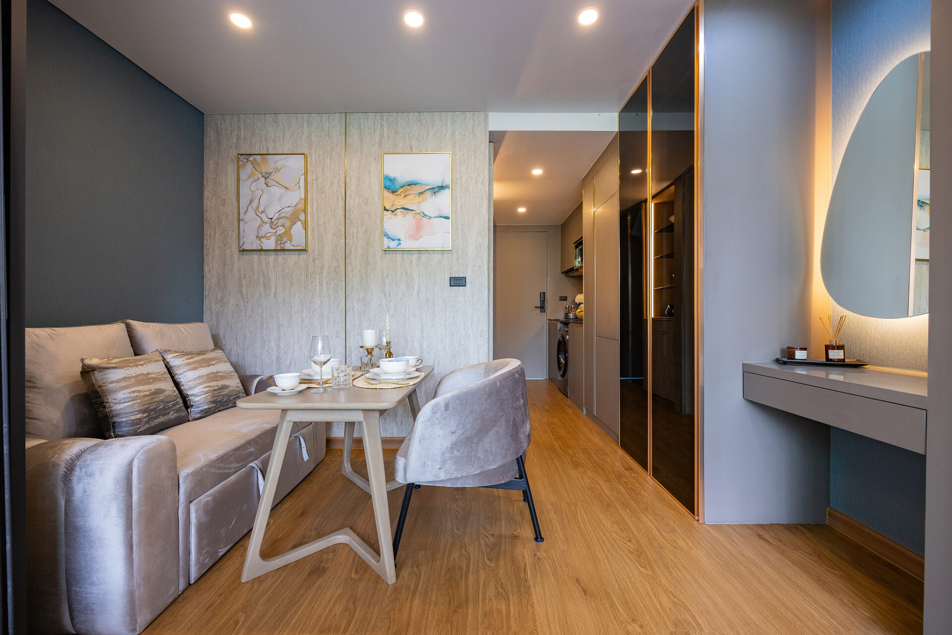 Open-plan living area with a beige sofa, decorative cushions, and a light wood dining table set for four in a contemporary apartment.