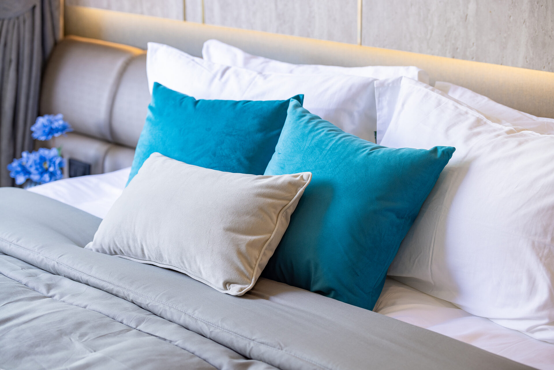 A neatly made bed with white sheets and blue and beige throw pillows under warm ambient lighting.