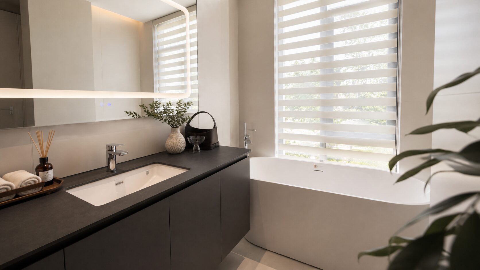 Modern bathroom with dark vanity, white undermount sink, chrome faucet, and decorative items on countertop beside a freestanding white tub by large striped blinds.