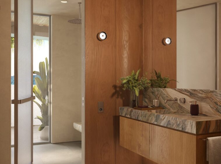 Modern bathroom with warm wood cabinets, marble countertop, and potted plants; shower area visible in back.