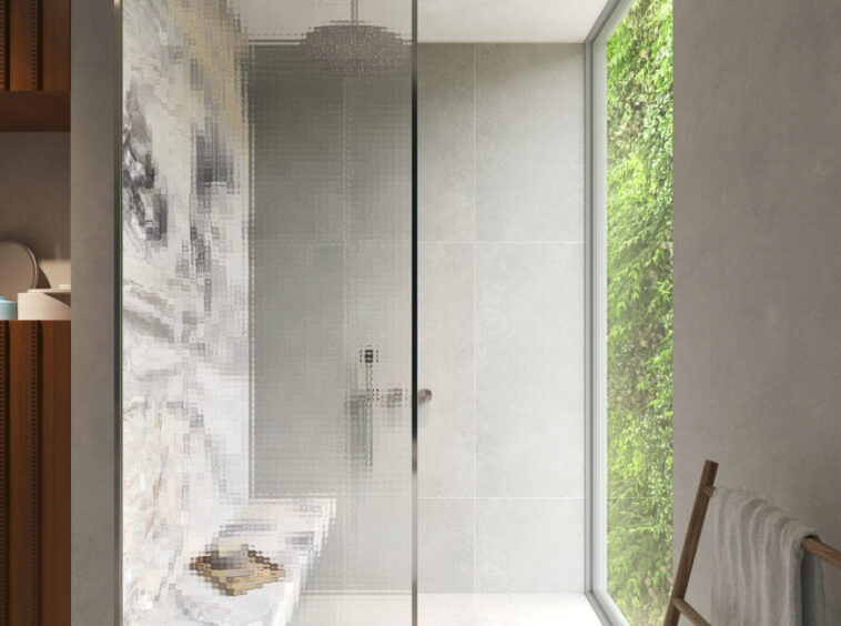 Modern bathroom with a glass shower door, grey tiled walls, and a large window overlooking greenery to the right.