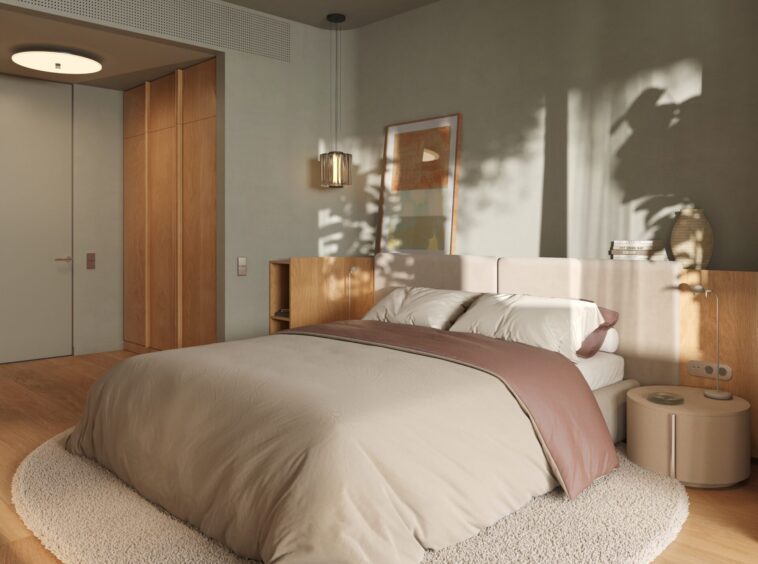 Modern bedroom with a low beige bed, circular shag rug, light wood floors, a nightstand with a lamp, and framed artwork on the wall illuminated by natural light.