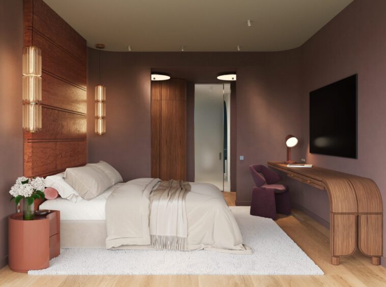 Modern hotel bedroom with a large bed, beige bedding, and a pink side table with flowers on the left; purple walls and wooden accents create a warm look.