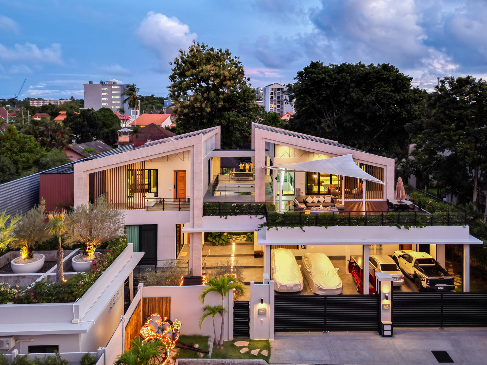 Aerial view of a contemporary residential complex with angular white buildings, outdoor living areas, palm trees, and parked cars at dusk.