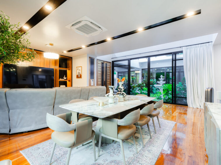 Open-plan living and dining area with a marble table, gray sofa, and large glass doors opening to a garden.