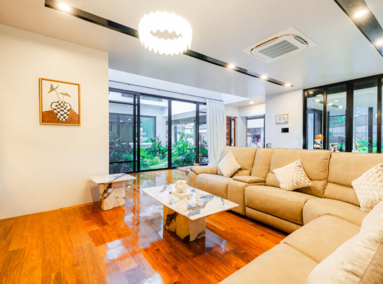 Bright modern living room with a beige sectional, marble-topped coffee tables, and large glass doors opening to a garden.