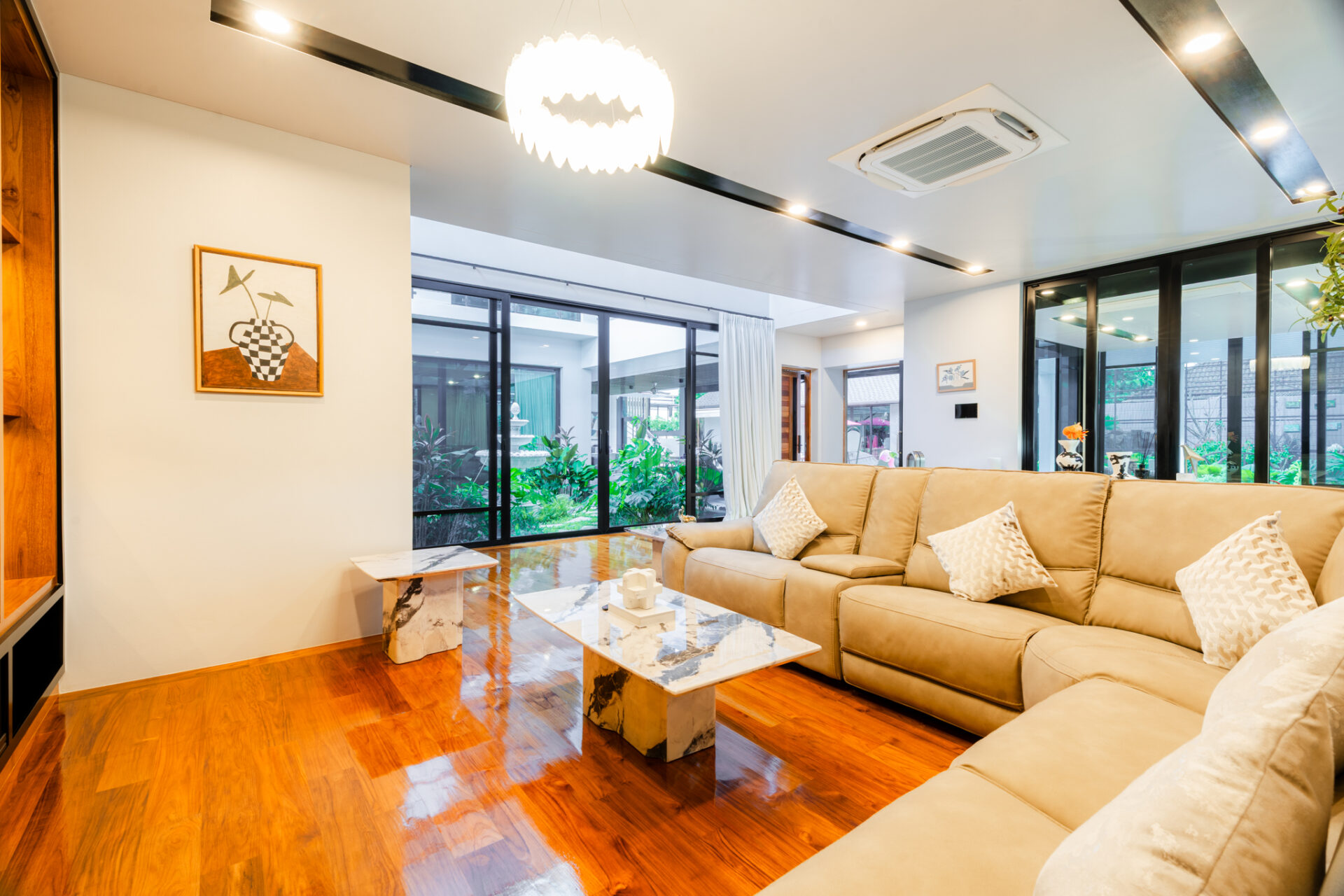 Bright modern living room with a beige sectional, marble-topped coffee tables, and large glass doors opening to a garden.