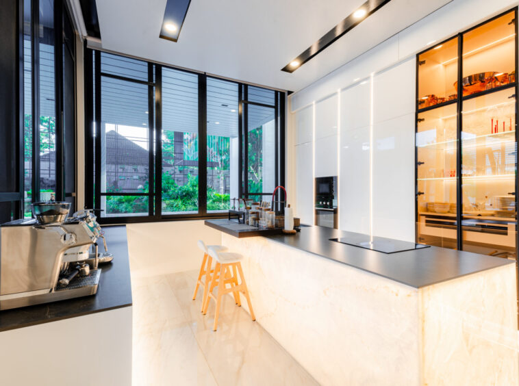 Modern kitchen with marble island, espresso machine, and built-in oven by glass-front cabinets.