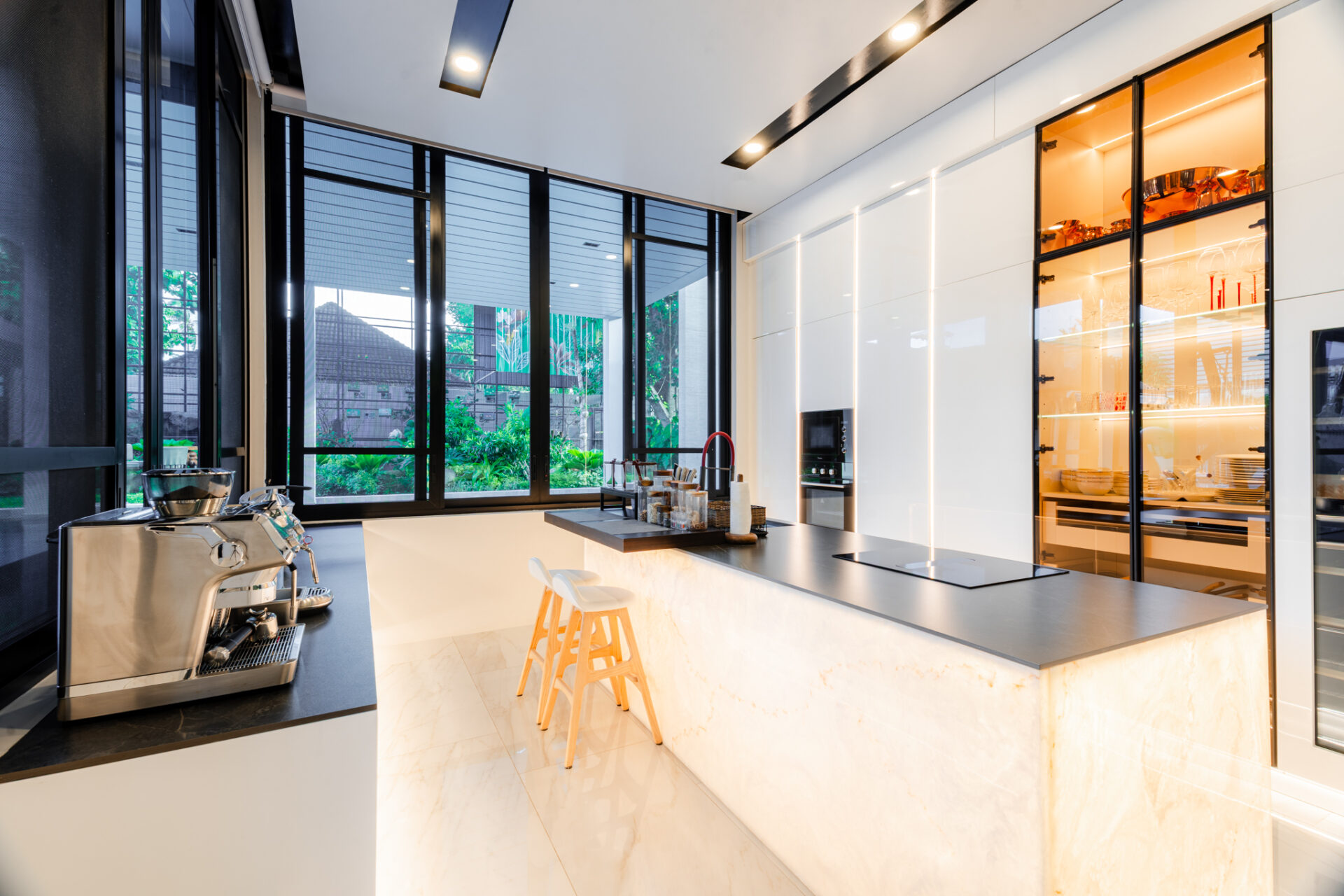 Modern kitchen with marble island, espresso machine, and built-in oven by glass-front cabinets.
