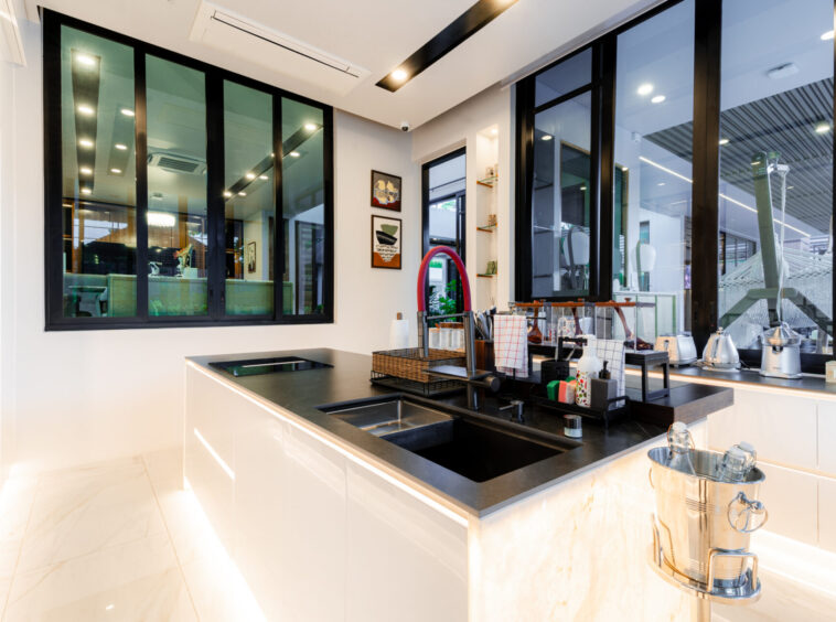 Bright modern kitchen with white glossy cabinets, black countertop, and a central island featuring a sink and cookware rack.