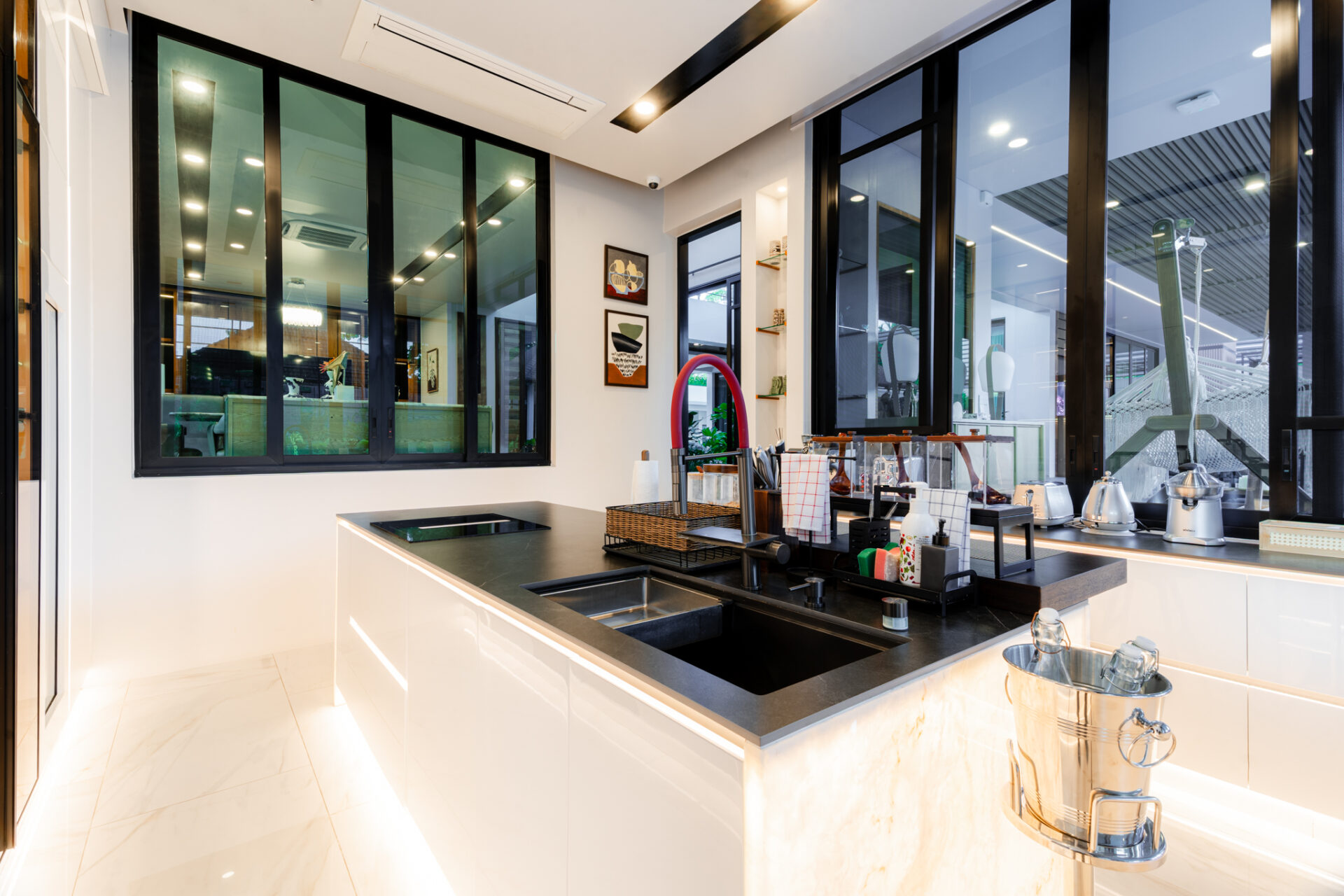 Bright modern kitchen with white glossy cabinets, black countertop, and a central island featuring a sink and cookware rack.