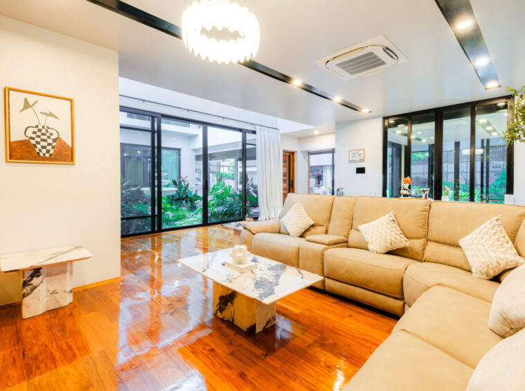 Bright living room with a beige sectional sofa, marble coffee tables, and large glass doors opening to a garden.