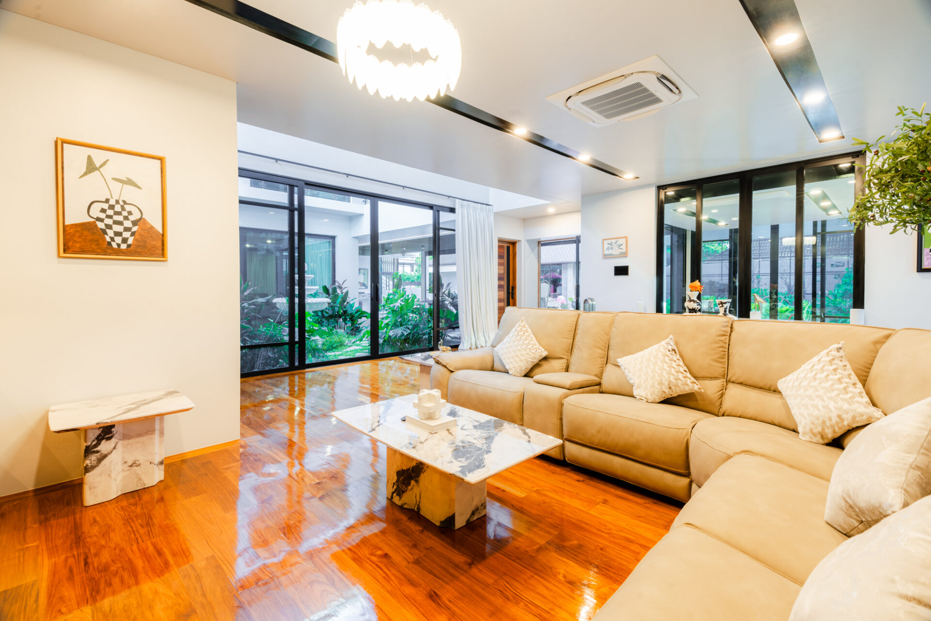 Bright living room with a beige sectional sofa, marble coffee tables, and large glass doors opening to a garden.