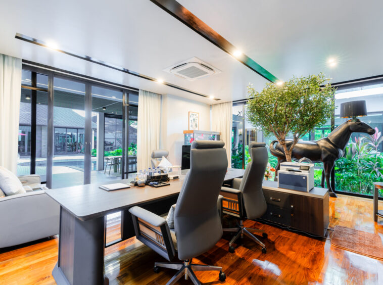 Modern office with a long desk, black ergonomic chairs, and a life-size black horse statue among lush plants by large glass walls.