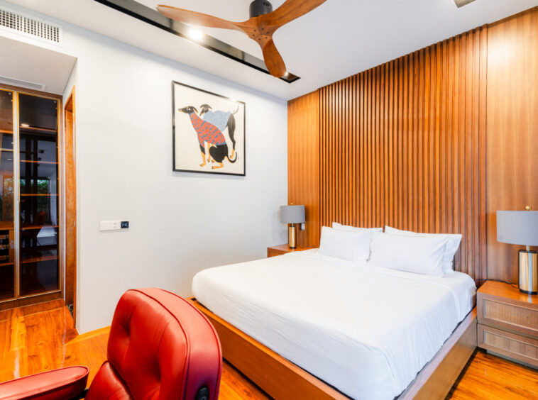 Bedroom with white bedding, wood slat accent wall, matching nightstands and lamps; red leather chair in foreground.