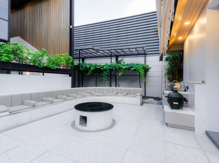 Modern outdoor courtyard with built-in curved seating around a circular fire pit and greenery along a trellis wall.