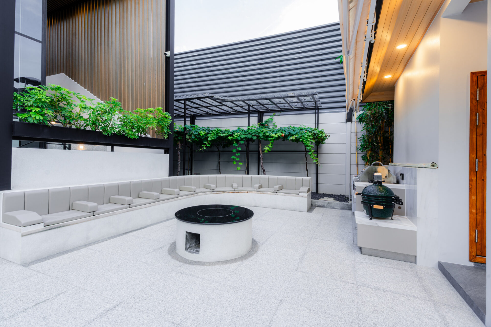 Modern outdoor courtyard with built-in curved seating around a circular fire pit and greenery along a trellis wall.
