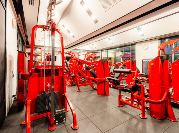 Red multi-station strength training machines in a bright gym.