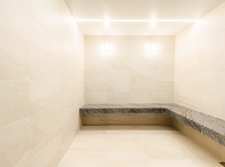 Empty marble-clad elevator interior with a dark marble bench along the back wall and bright ceiling lights.