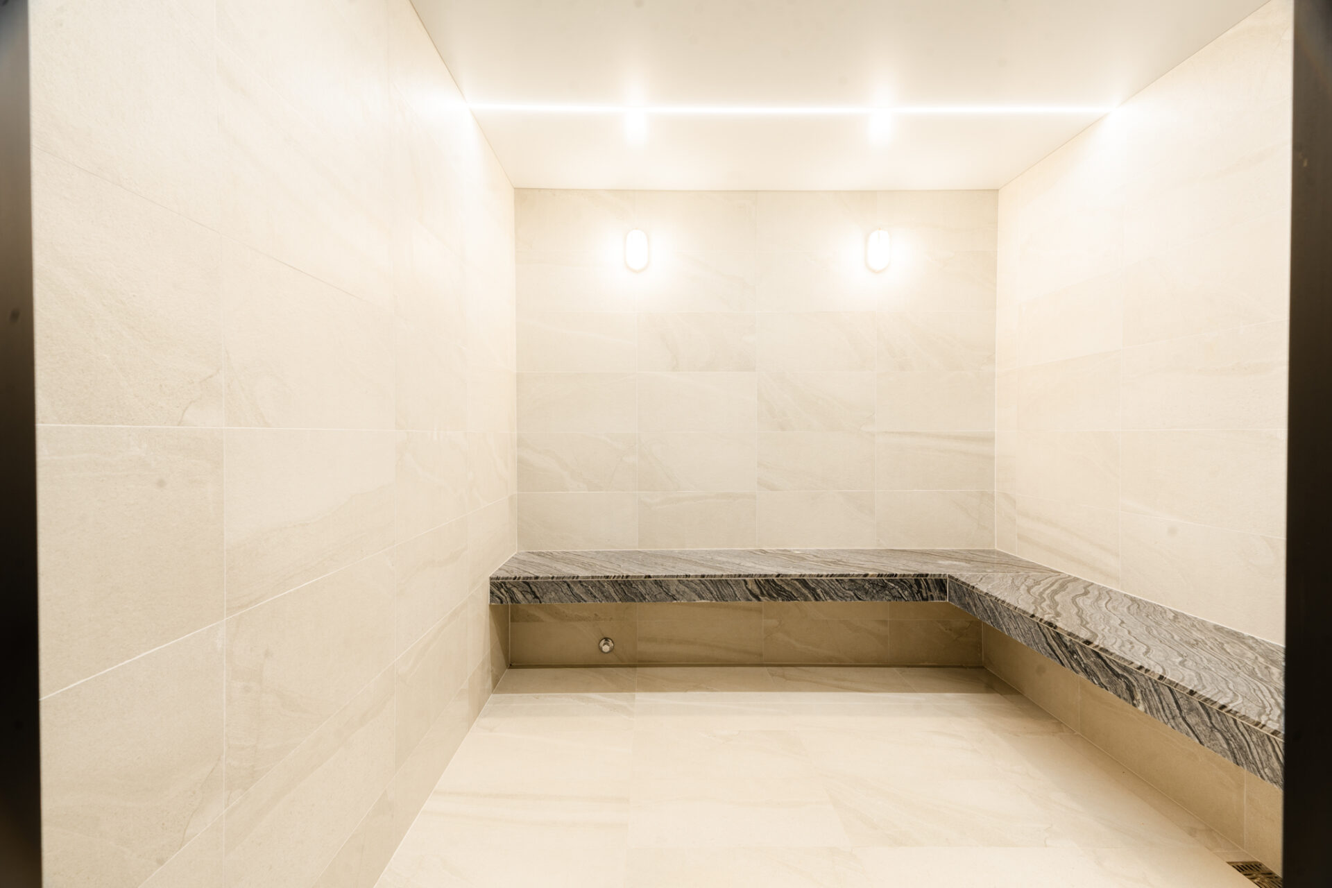 Empty marble-clad elevator interior with a dark marble bench along the back wall and bright ceiling lights.