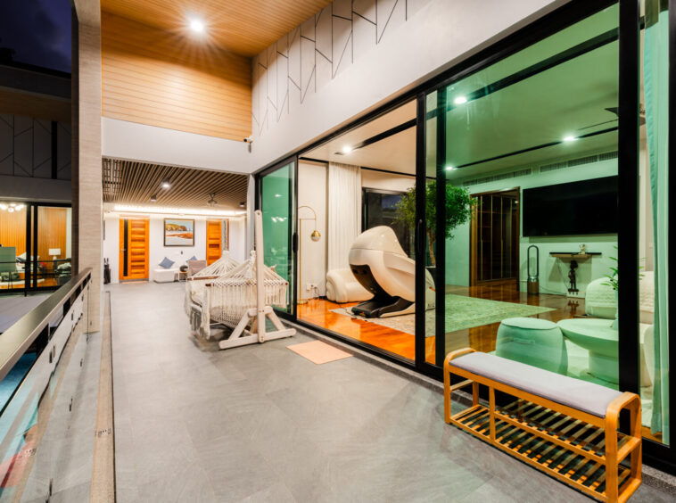 Modern indoor-outdoor living space with large glass walls, hammocks, and a white spa chair in a bright living area.
