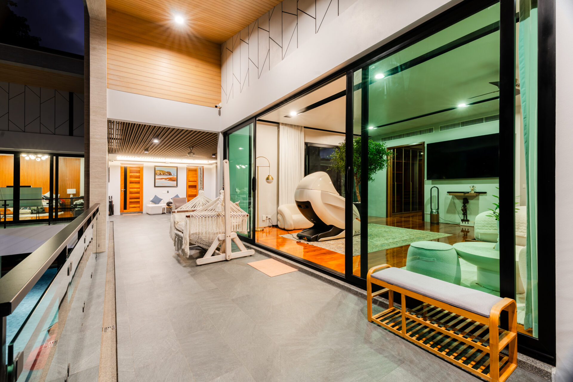 Modern indoor-outdoor living space with large glass walls, hammocks, and a white spa chair in a bright living area.