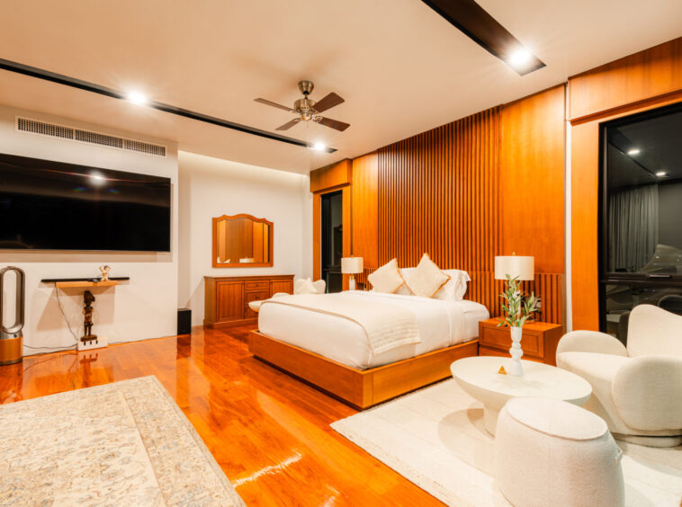 Luxurious hotel bedroom with a large bed, wood panel accents, and a wall-mounted flat-screen TV visible across the room.