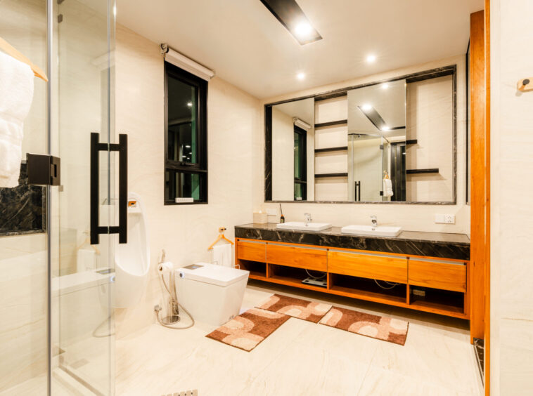 Wide view of a modern bathroom with a double-sink vanity, large framed mirror, and glass shower enclosure in warm lighting.