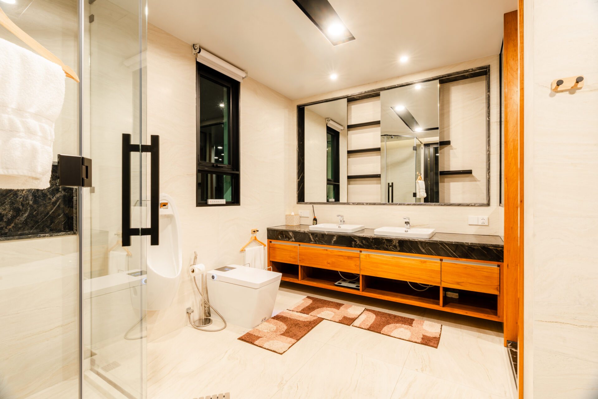 Wide view of a modern bathroom with a double-sink vanity, large framed mirror, and glass shower enclosure in warm lighting.