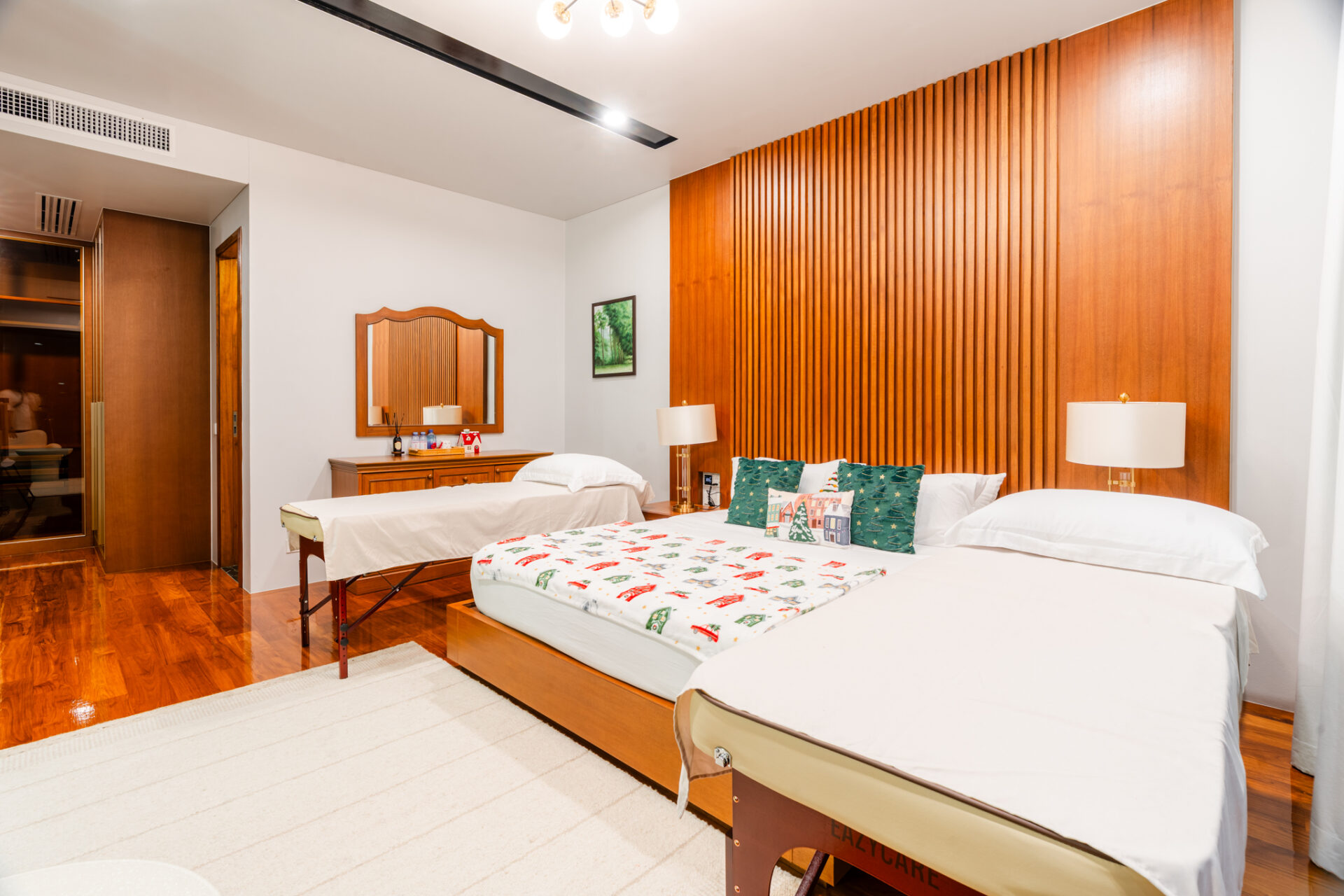 Hotel room with two queen beds, Christmas-themed throws and pillows, and a tall wooden headboard wall