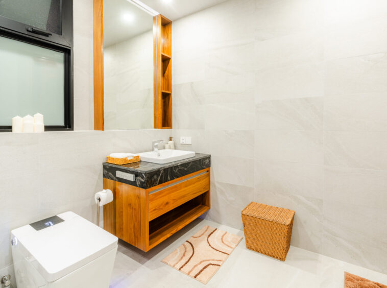 Modern bathroom with a wooden vanity, marble countertop, large mirror, and beige tiled walls; a wicker basket sits nearby.