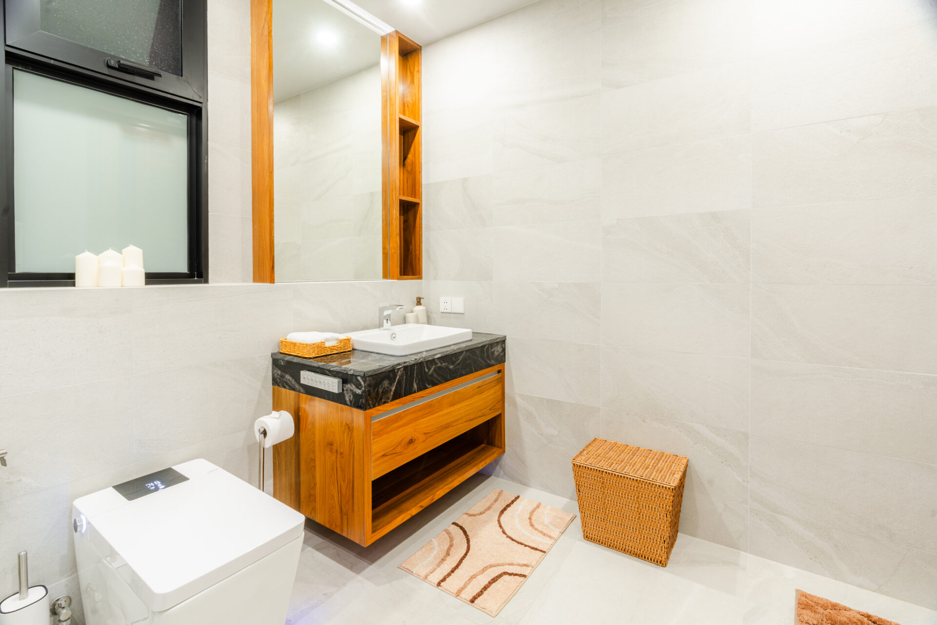 Modern bathroom with a wooden vanity, marble countertop, large mirror, and beige tiled walls; a wicker basket sits nearby.