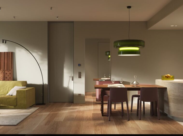 Open-plan living and dining area with a green sectional sofa, abstract art, and a curved floor lamp beside a doorway, leading to a modern kitchen island.