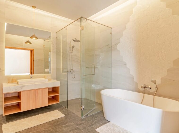 Bright modern bathroom featuring a glass-enclosed shower, freestanding tub, and a light wood vanity with marble countertop.
