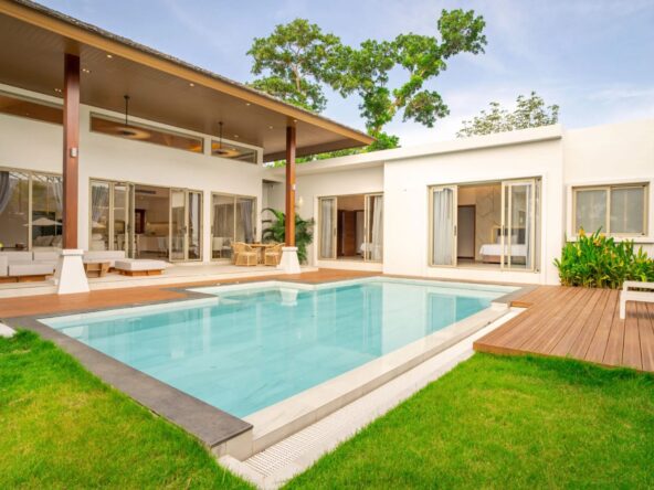 Modern white villa with a rectangular pool, wooden deck, and open living spaces by glass doors right outside the home.