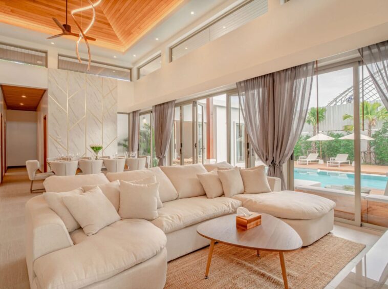 Bright open-plan living room with a large white sectional sofa and glass doors overlooking a pool area.