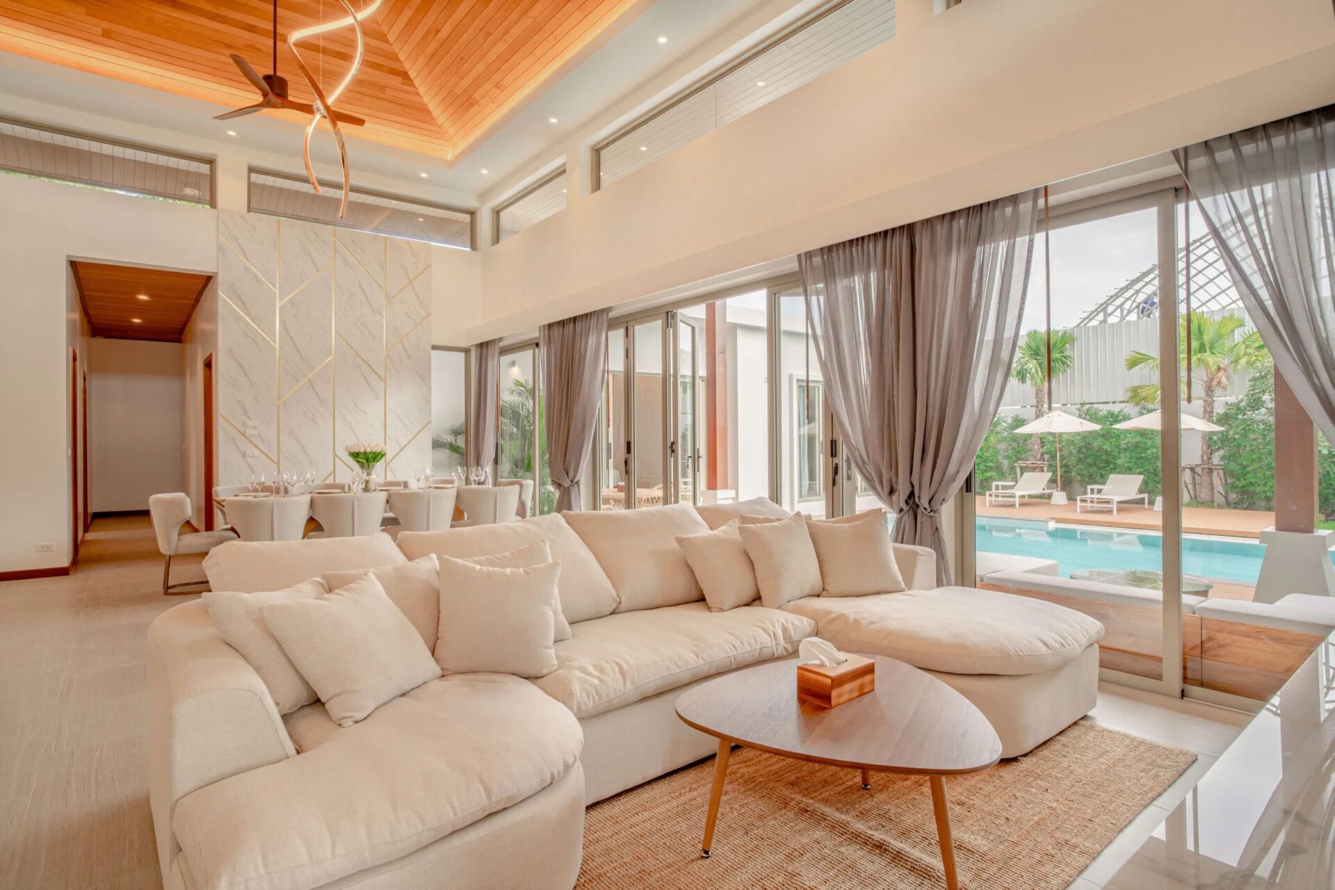 Bright open-plan living room with a large white sectional sofa and glass doors overlooking a pool area.